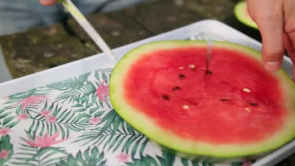 Jonge man snijdt mes in plakjes, grote rijpe rode watermeloen, op straat, zonnige dag — Stockvideo