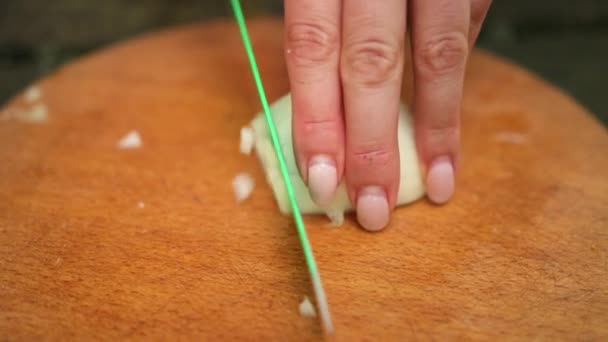 女性は木製の板、緑のナイフ、玉ねぎの小片に切り取ります — ストック動画