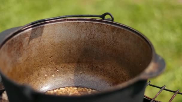 Hombre arroja condimento rojo, en una olla grande de hierro fundido en la que las cebollas fritas — Vídeos de Stock