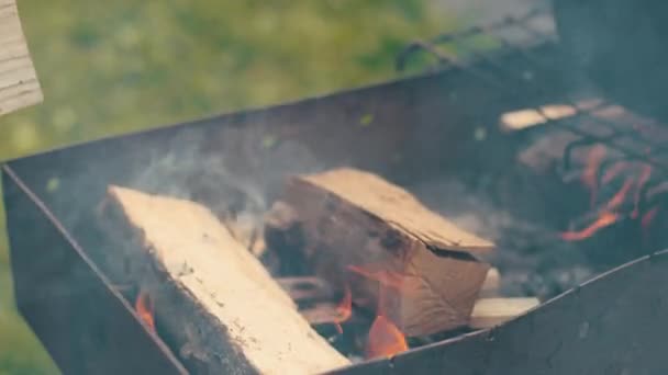 Chlap hází málo dřeva do grilu, zapálil malý oheň, odpoledne na ulici — Stock video