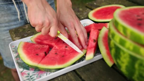 Jonge man snijdt mes in plakjes, grote rijpe rode watermeloen, op straat, zonnige dag — Stockvideo