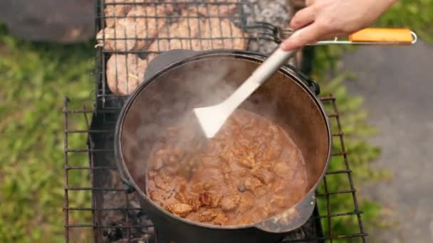 In large cast iron pot preparing dish, red with meat onions and other components — Stock Video