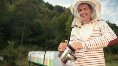 özel giysiler içinde insan arıcı, arılar sakin leştirmek için bir sigara içen tutarak