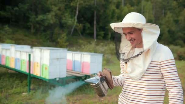 Apicultor homem em roupas especiais, segurando um fumante para acalmar abelhas, um monte de fumo — Vídeo de Stock