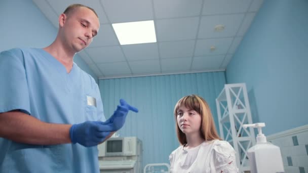 Doktor nosí rukavice na jedno použití, pacientka sedí a čeká na zkoušky — Stock video