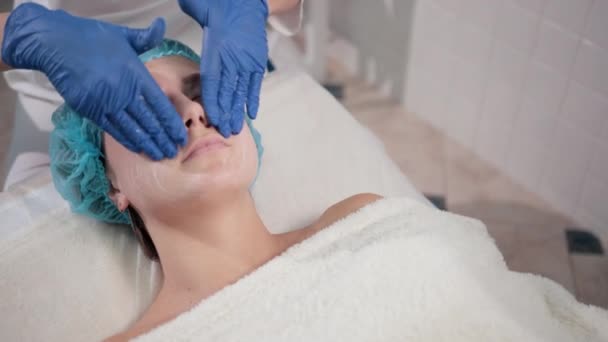 Ošetřovatelka v modrých rukavicích, dělá ženskou masáž obličeje se světlými pohyby — Stock video