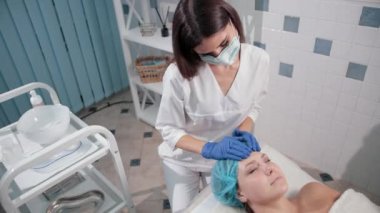 mavi eldiven hemşire doktor, ışık hareketleri ile bir kadın yüz masajı yapar
