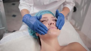 mavi eldiven hemşire doktor, ışık hareketleri ile bir kadın yüz masajı yapar