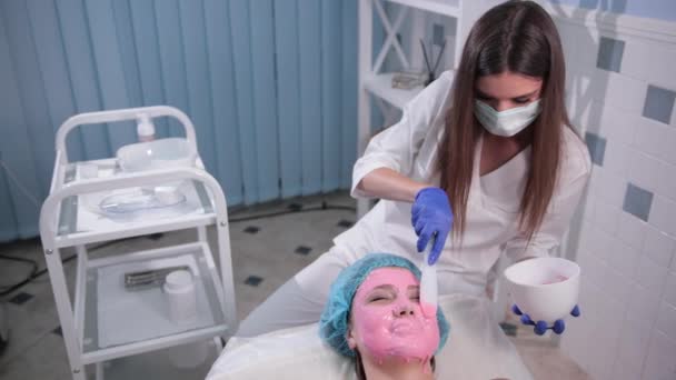 Enfermeira médico faz mulher massagem facial, faz com que a máscara rosa com escova — Vídeo de Stock