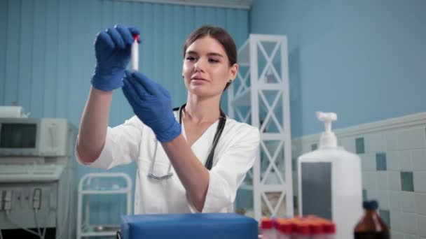 Médico enfermeira segurando um tubo de ensaio, examina cuidadosamente — Vídeo de Stock
