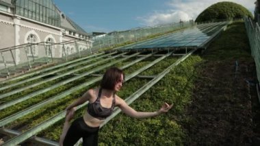 Siyah spor kıyafetli genç kız dışarıda yoga yapıyor, çeşitli egzersizler yapıyor.