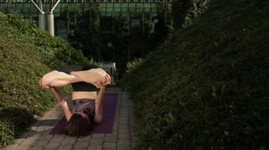 Siyah spor kıyafetli genç kız dışarıda yoga yapıyor, çeşitli egzersizler yapıyor.