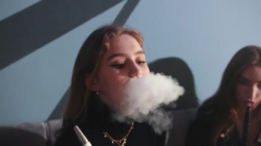 Kafede oturmuş nargile içen iki genç kız. Bir sürü kalın duman.