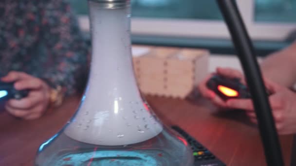 deux jeunes hommes assis dans un café à la table de jeu console et fumer un narguilé 