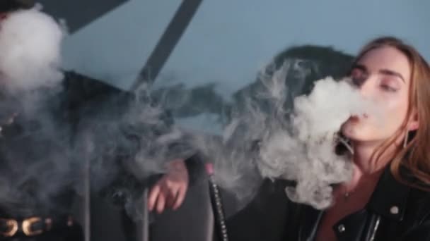 Dos chicas jóvenes sentadas en la cafetería fumando una cachimba. mucho humo espeso — Vídeo de stock