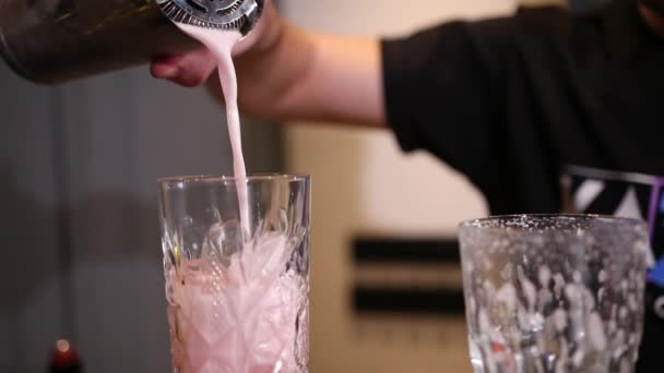 Camarero con una coctelera vierte un cóctel rosa en un vaso grabado con hielo — Vídeo de stock