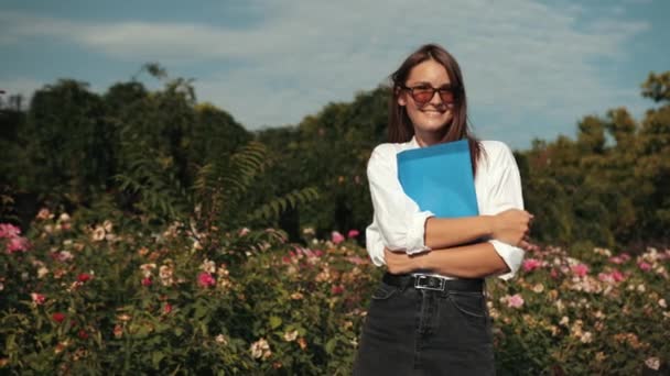 Joven, con gafas sosteniendo carpeta azul, posando para la cámara en la calle — Vídeo de stock