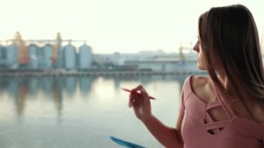 Pembe elbiseli genç kız, elinde mavi dosya ve kalem, yazıyor ve sayıyor.