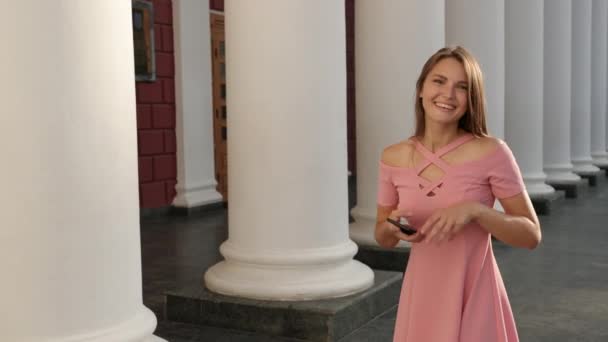 Νεαρό κορίτσι κρατώντας smartphone, σε ροζ φόρεμα με τακούνια, αγαλλίαση και άλματα — Αρχείο Βίντεο