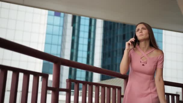 Menina segurando smartphone, em vestido rosa, emocionalmente falando e acenando com as mãos — Vídeo de Stock