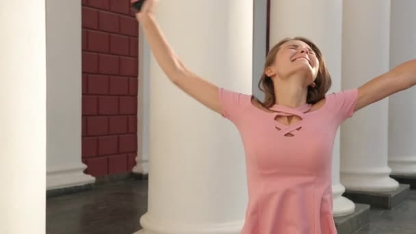 Jeune fille tenant smartphone, en robe rose avec talons, se réjouit et saute — Video