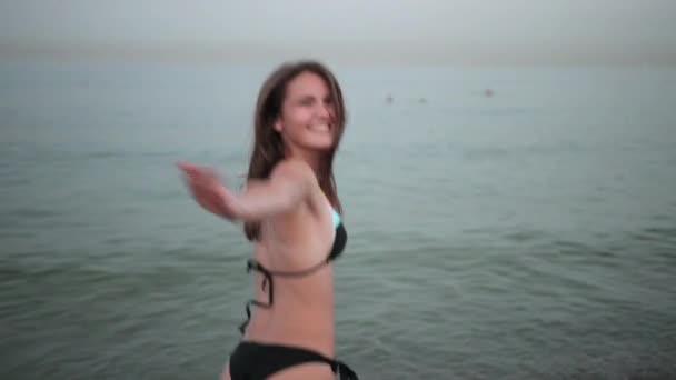 Young girl in black swimsuit, spinning around and posing for camera on beach — Stock Video