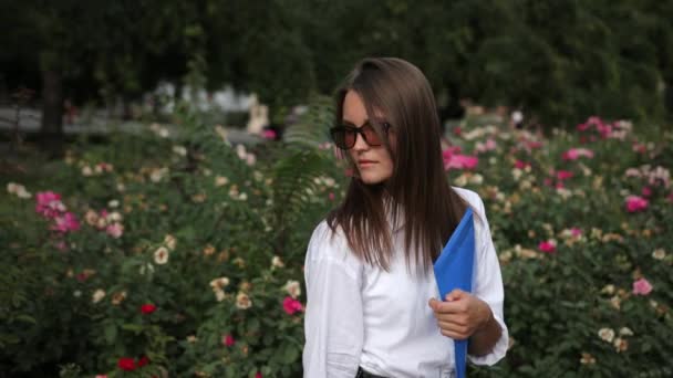 Joven, con gafas sosteniendo carpeta azul, posando para la cámara en la calle — Vídeos de Stock