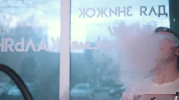 Mladý muž v bílém tričku sedí v kavárně u stolu Kouření hookah — Stock video