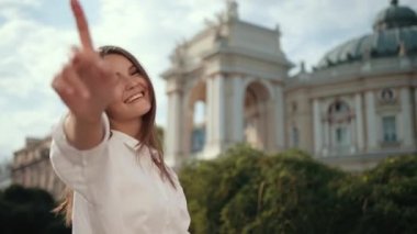 Beyaz bluzlu genç kız, kameranın önünde gülümseyerek poz veriyor.