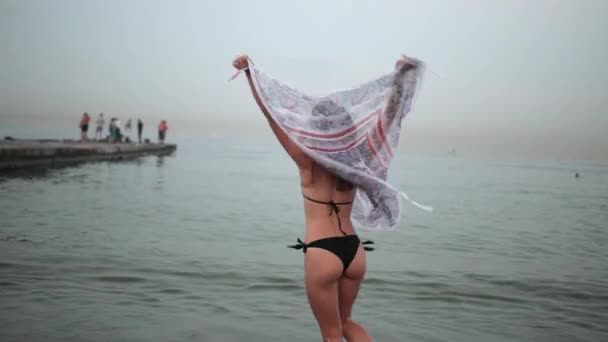 Girl in black swimsuit, holding pareo, spinning around and posing on beach — Stock Video