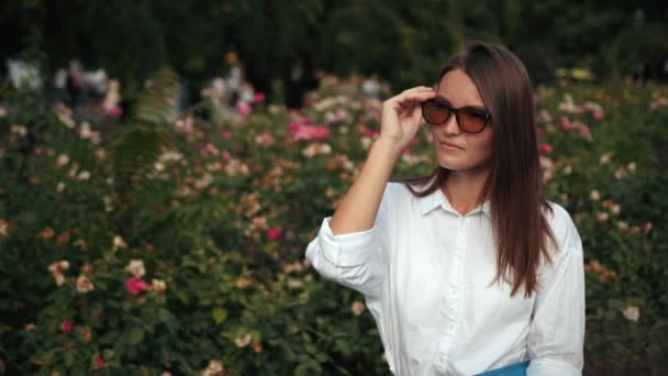 Young girl, wearing glasses holding blue folder, posing for camera on street — Stock Video