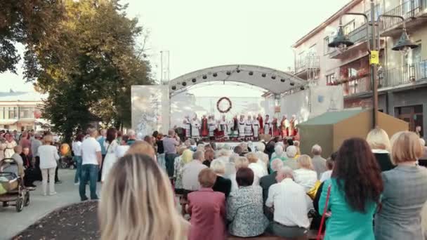 På vita scenen uppträder människor, kvinnor och män i folkdräkter, sjunger och dansar — Stockvideo