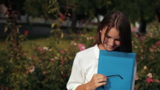 파란 폴더를 든 안경을 쓴 소녀, 거리에서 카메라 포즈를 취하는 모습 — 비디오