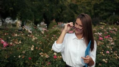 Mavi klasör tutan gözlüklü genç kız, sokakta kameraya poz veriyor.