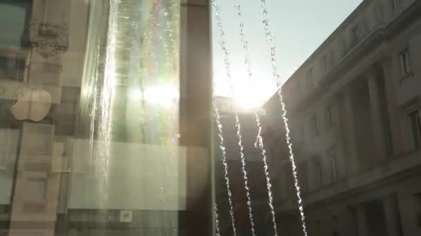 Straßenbrunnen. Wasserstrahlen sprühen nach oben, fallen auf Glas, dahinter scheint die Sonne — Stockvideo