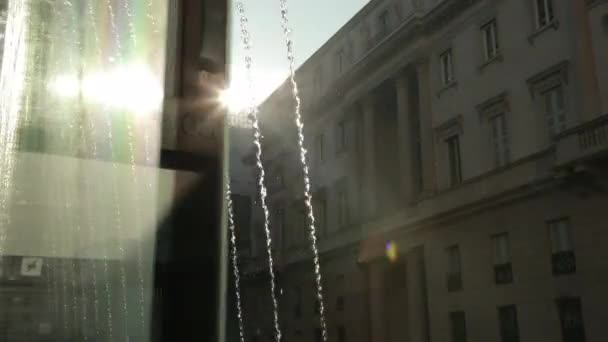 Straßenbrunnen. Wasserstrahlen sprühen nach oben, fallen auf Glas, dahinter scheint die Sonne — Stockvideo
