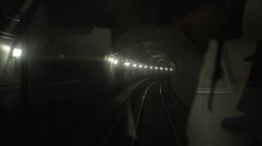 Karanlık yeraltı tren tüneli, derinlerde, metro vagonu raylarda ilerliyor.