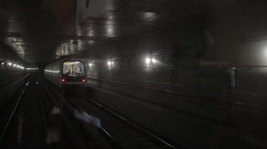Karanlık yeraltı tren tüneli, derinlerde, metro vagonu raylarda ilerliyor.