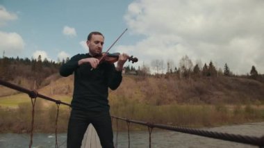 Köprüde kemancı, sokak sanatçısı, dışarıda keman çalıyor. hızlı nehir