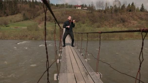 Pemain biola di jembatan, pemain jalanan bermain biola, di luar. sungai cepat — Stok Video