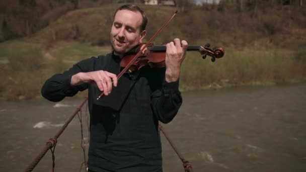 Geiger auf der Brücke, Straßenkünstler, der Geige spielt, draußen. Schneller Fluss — Stockvideo