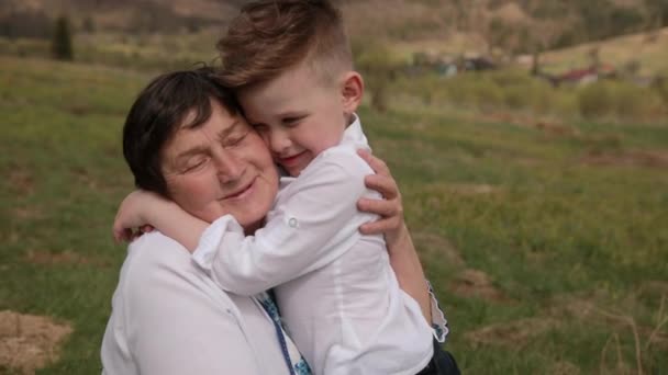 El nieto se acerca a la abuela. Él pone su brazo alrededor de su cuello. amor gran — Vídeos de Stock