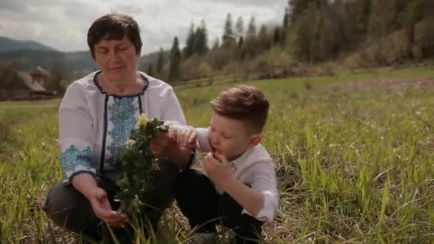 Großmutter macht mit ihrem kleinen Enkel einen Kranz aus Wildblumen. Draußen entspannen — Stockvideo