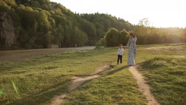 Женщина гуляет с сыном по парку, путешествует дети, ребенок держит маму за руку — стоковое видео