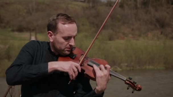 Houslista na mostě, pouliční herec na housle, venku. rychlá řeka — Stock video