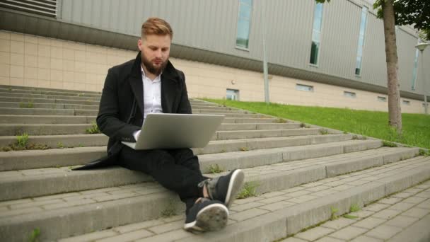 Красивий елегантний чоловік працює надворі, зосереджений ноутбук, насолоджується, бородатий хіпстер — стокове відео