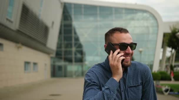 Ένας άντρας μιλάει στο τηλέφωνο έξω, όμορφος νεαρός επιχειρηματίας, απαντά στο smartphone — Αρχείο Βίντεο