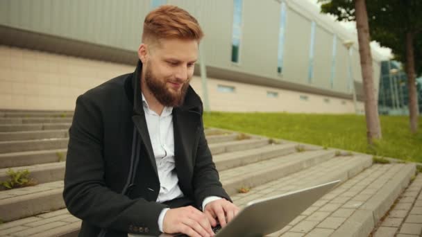 Hombre elegante guapo trabajando fuera, portátil enfocado, disfrutando, hipster barbudo — Vídeos de Stock