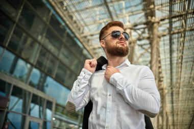 Yakışıklı genç bir adam, şehir sokaklarında ceketini omzuna asmış yürüyor.