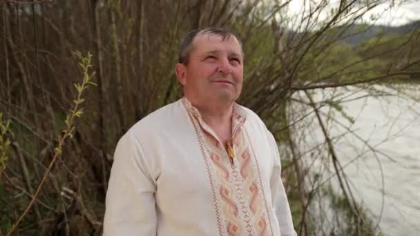 Alter Großvater älterer Herr steht am Ufer des Flusses in einem bestickten — Stockvideo